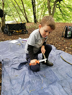A child sharpens a stick with a knife